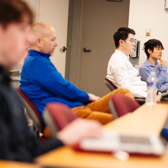 Group of men sitting at desks, some out of focus looking towards the right