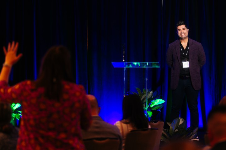 Man on stage looking at audience member with hand up.