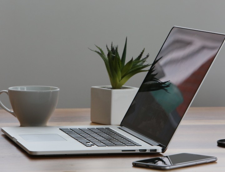 Remote work scene with a laptop, coffee cup, cell phone, and plant on desk or table.