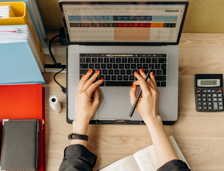 Hands on laptop using spreadsheet with binders and calculators on the desk around.